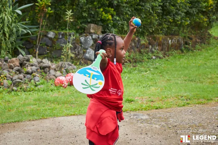 Une petite fille brandit une balle et une raquette en plein jeu