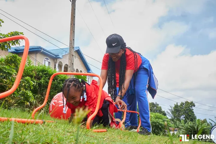 Une petite fille passe sous des arceaux, encouragée par une monitrice