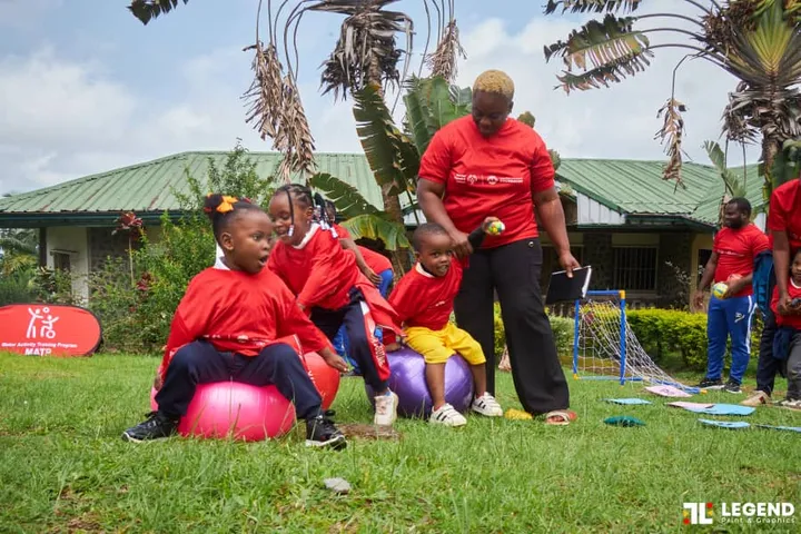 De jeunes enfants en tee-shirts rouges assis sur des ballons de gym, encadrés par une monitrice