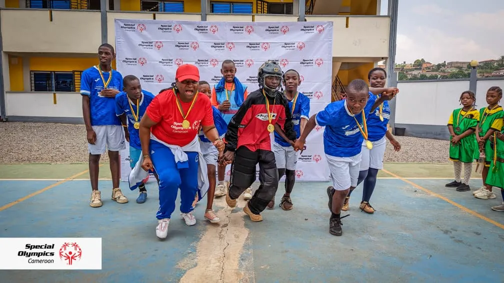 Équipe de floorball médaillée s’élançant en ligne devant un mur aux couleurs de Special Olympics Cameroun