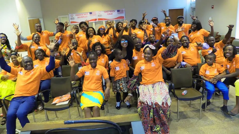 Participants du Forum de Santé des Familles en polos orange, bras levés dans la salle
