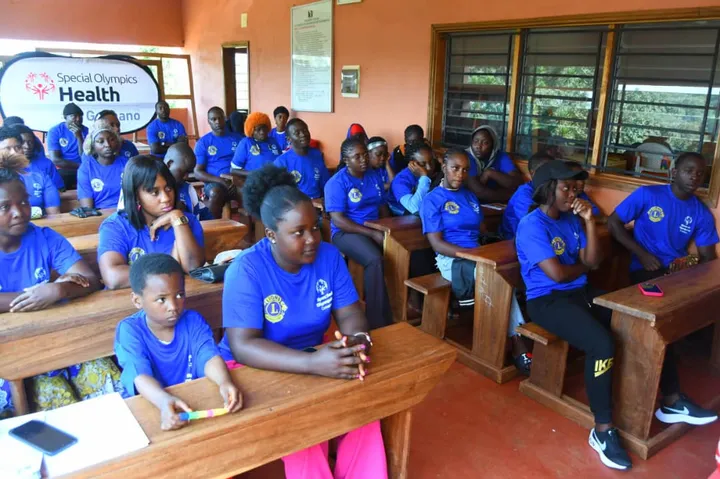 Jeunes et adultes en tee-shirts bleus assis à des pupitres dans une salle de classe
