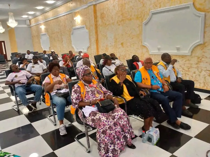 Participants assis dans une grande salle, certains en gilets jaunes et orange