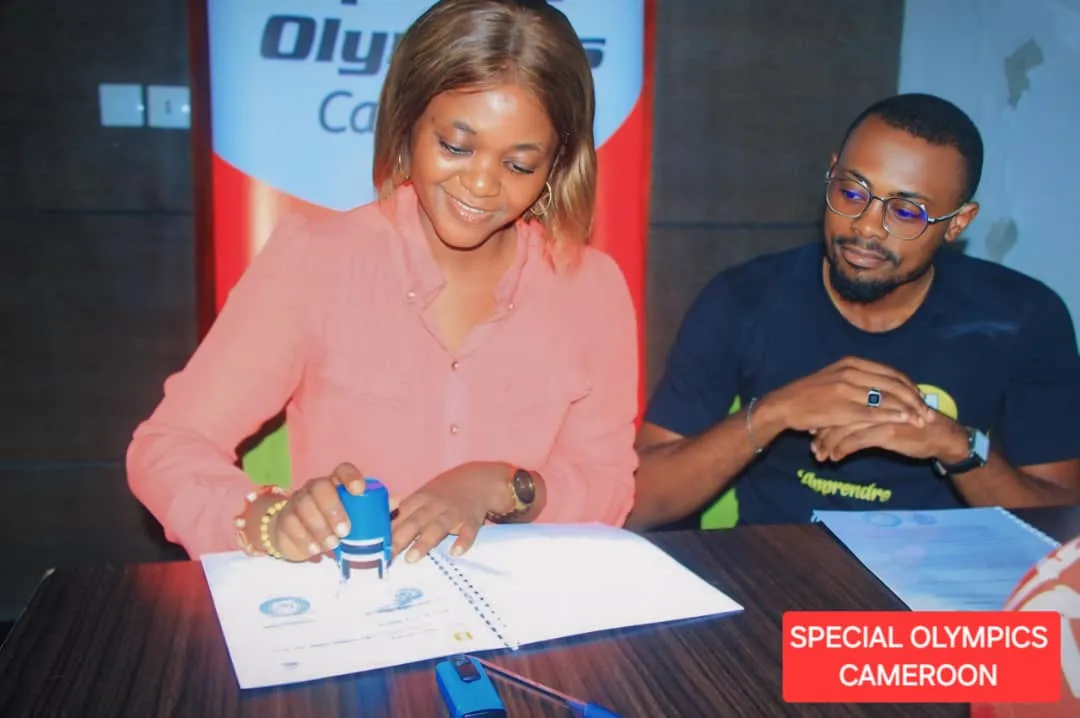 Une femme appose un cachet sur un document, devant une bannière de Special Olympics Cameroun