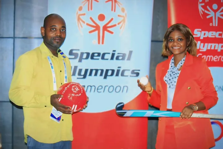 Un homme et une femme tiennent un ballon et une crosse de hockey devant une bannière de Special Olympics Cameroun
