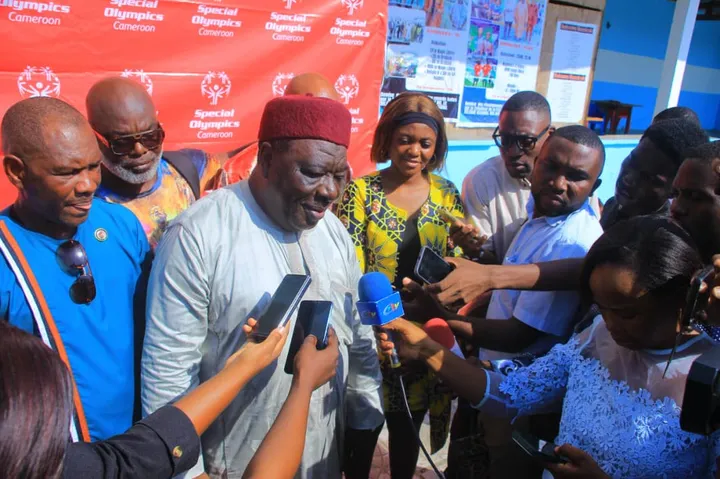 Une personnalité répond à la presse devant un mur aux couleurs de Special Olympics Cameroun