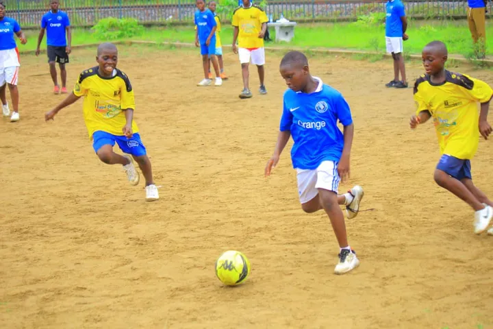 Jeunes footballeurs en maillots jaunes et bleus disputant le ballon sur un terrain en sable